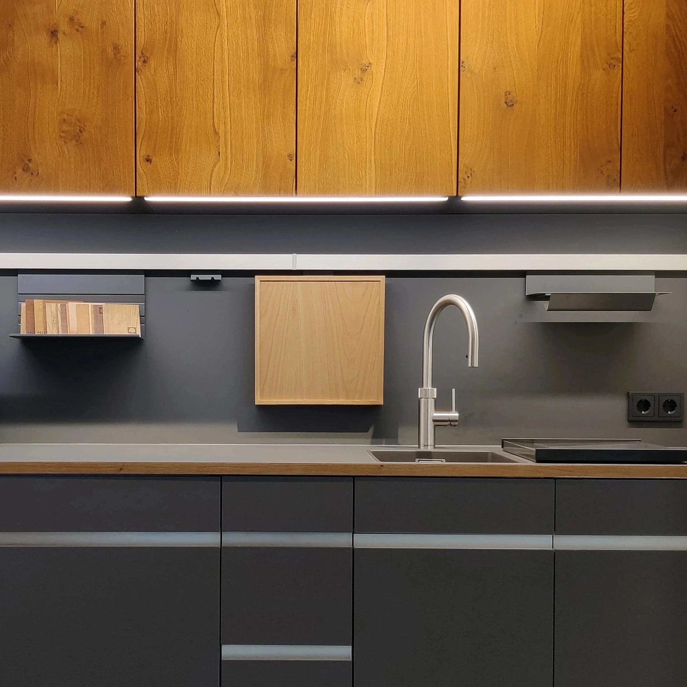 Teeküche mit Unterschränken aus anthrazit farbigem Fenix. Darüber Oberschränke mit Faltschiebetüren mit einer Front aus massiver, gebürsteter Wildeiche.