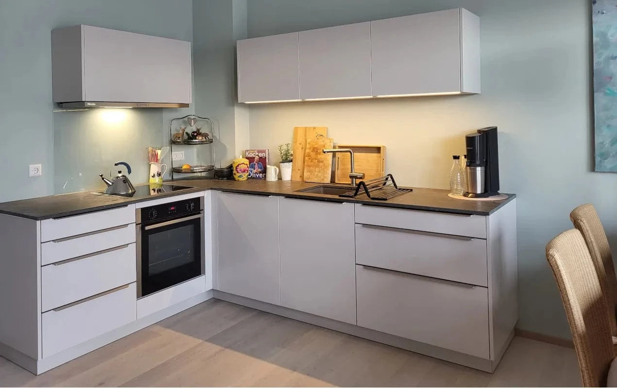 Moderne kleine Küche in L-Form, hellgrau mit schwarzer Stein-Arbeitsplatte und modernsten Küchengeräten von Miele