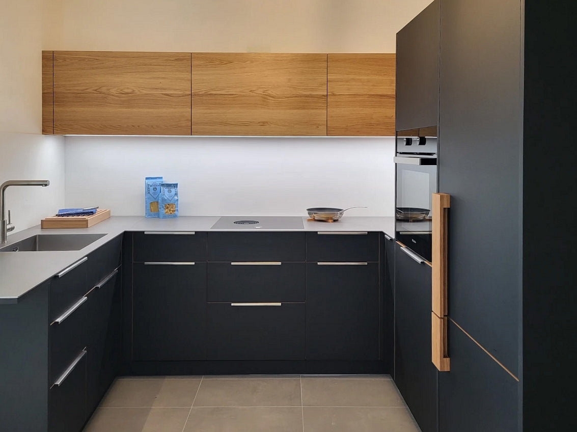 Eine kleine schwarze Küche in U-Form, kombiniert mit massivem Wildeiche-Holz und grauer hochwertiger Keramik von Dekton.